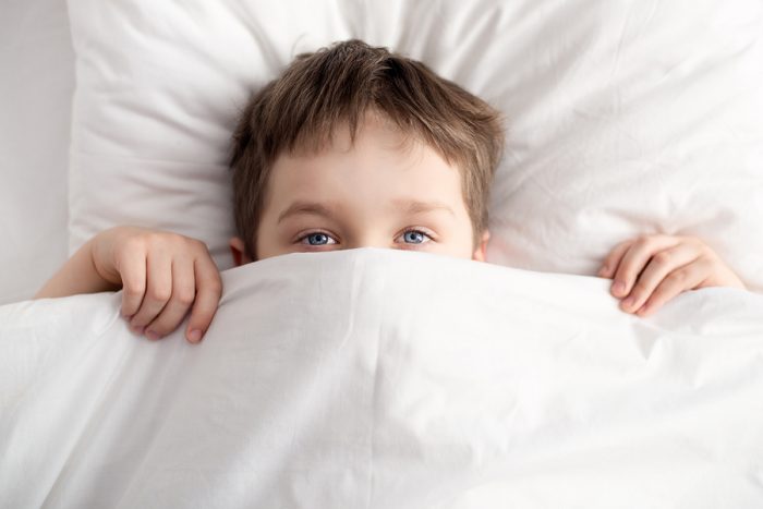 Top view of little boy in bed covering his face with white blanket or coverlet. Sleeping boy. Sleeping child